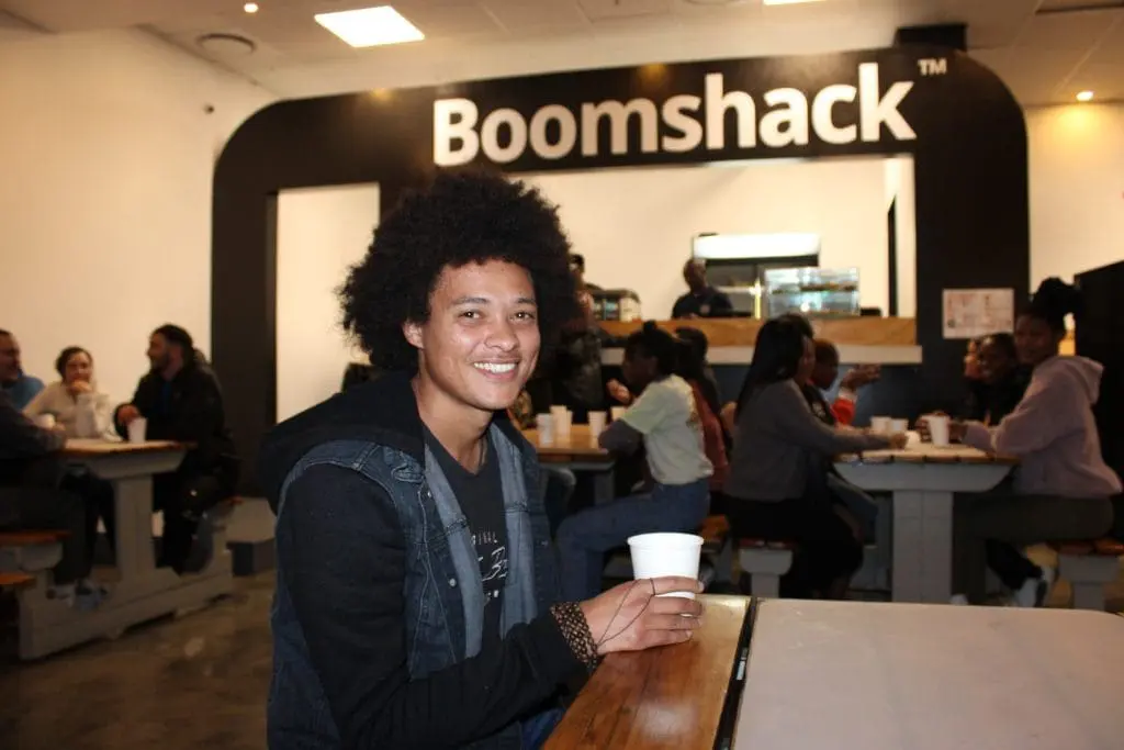 Guy with afro sitting in boomshack - coffee counter and other tables in background